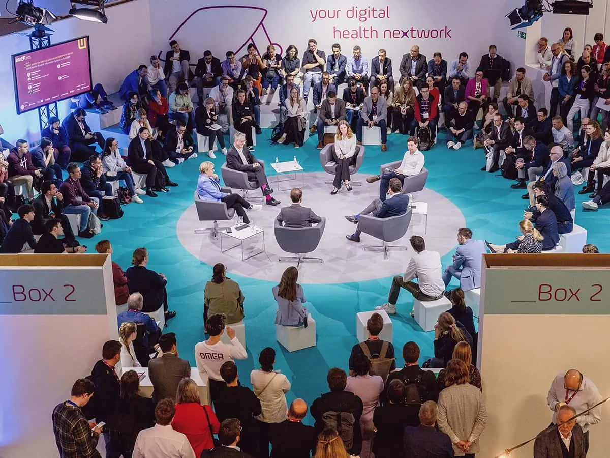 Menschen sitzen im Kreis und schauen den Panelisten in der Mitte sitzend zu. Ansicht von oben