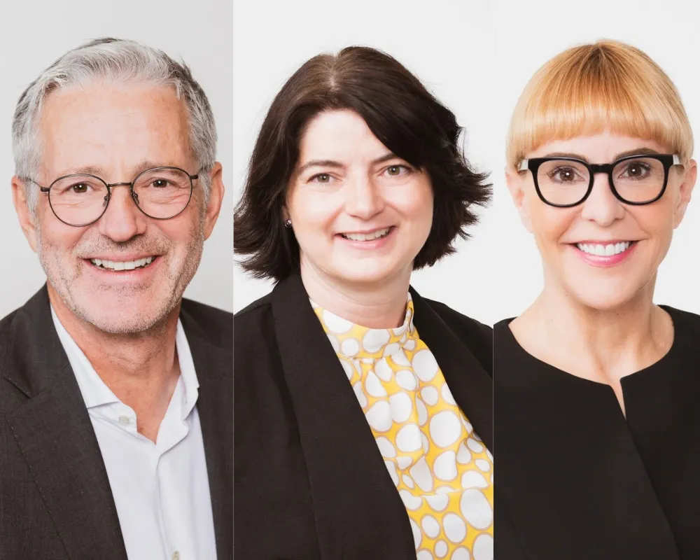 zwei Personen nebeneonander. Ein Mann links, in der Mitte eine Frau mit braunen Haaren und rechts eine Frau mit blonden Harren und einer Brille