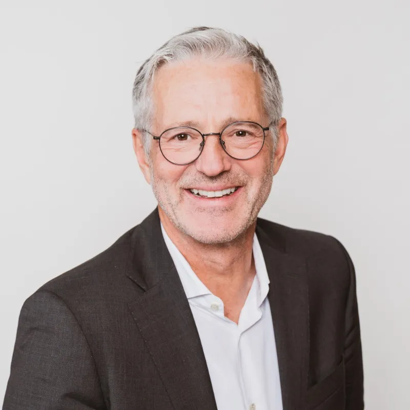 Mann mit graune haaren und runder dezenter Brille schaut lächelnd in die Kamera,